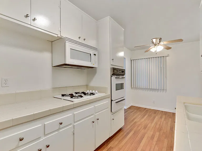 Kitchen with white gas cooktop over microwave, White Oven, Wood Style floors throughout dining area with ceiling fan