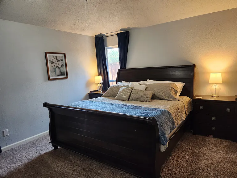 Primary suite features King bed, dresser, nightstands, mirror, TV and en suite bathroom w/ walk in closet. Private door to back patio and window.