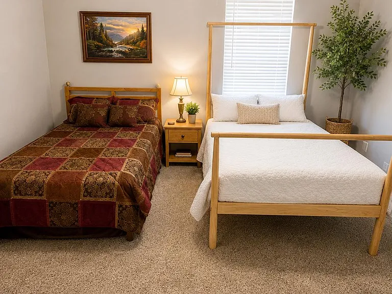 Well-sized bedroom with two beds, nightstand lighting, ceiling fan, and a window with blinds for comfortable daily living.