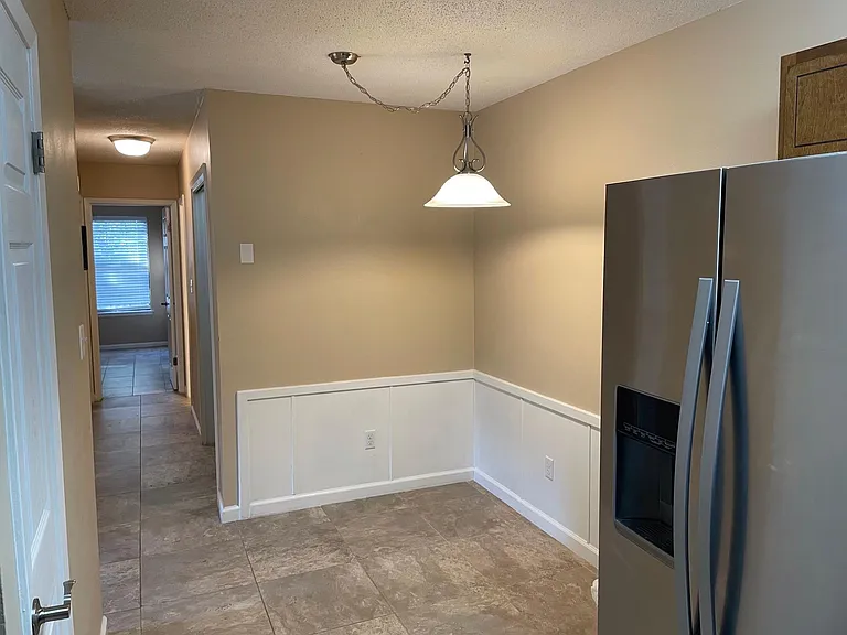 Dining nook and hallway to bedrooms also on left is pantry closet in kitchen and stainless steel refrigerator.