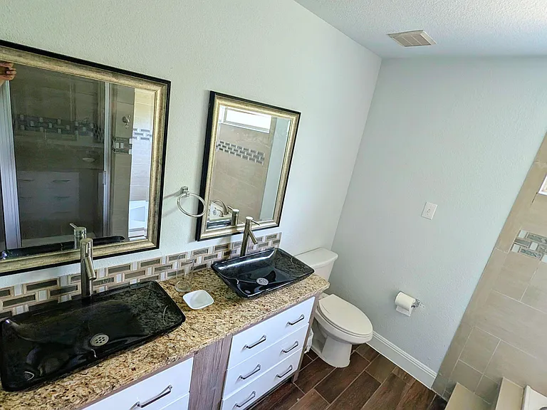 Bathroom with dual vessel sinks, granite vanity, framed mirrors, and a tiled shower surround with window.