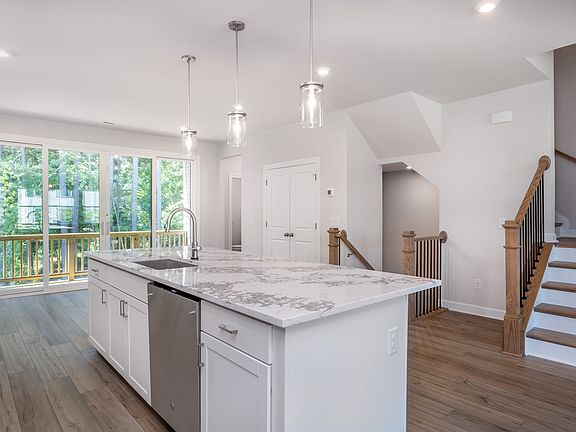 A modern, bright kitchen with white cabinets, marble countertops, and pendant lighting, set against