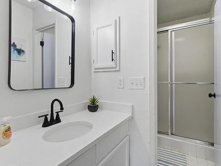 Updated bathroom with a wide vanity, modern black fixtures, ample mirror space, and a sliding glass tub/shower combo.