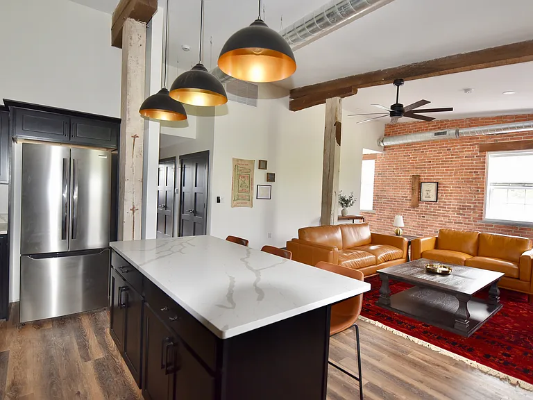 The living room features an open layout with optimal seating throughout, a desk/work space and a smart TV. The room features ceiling spotlights that are dimmable (its a whole mood) and a ceiling fan.