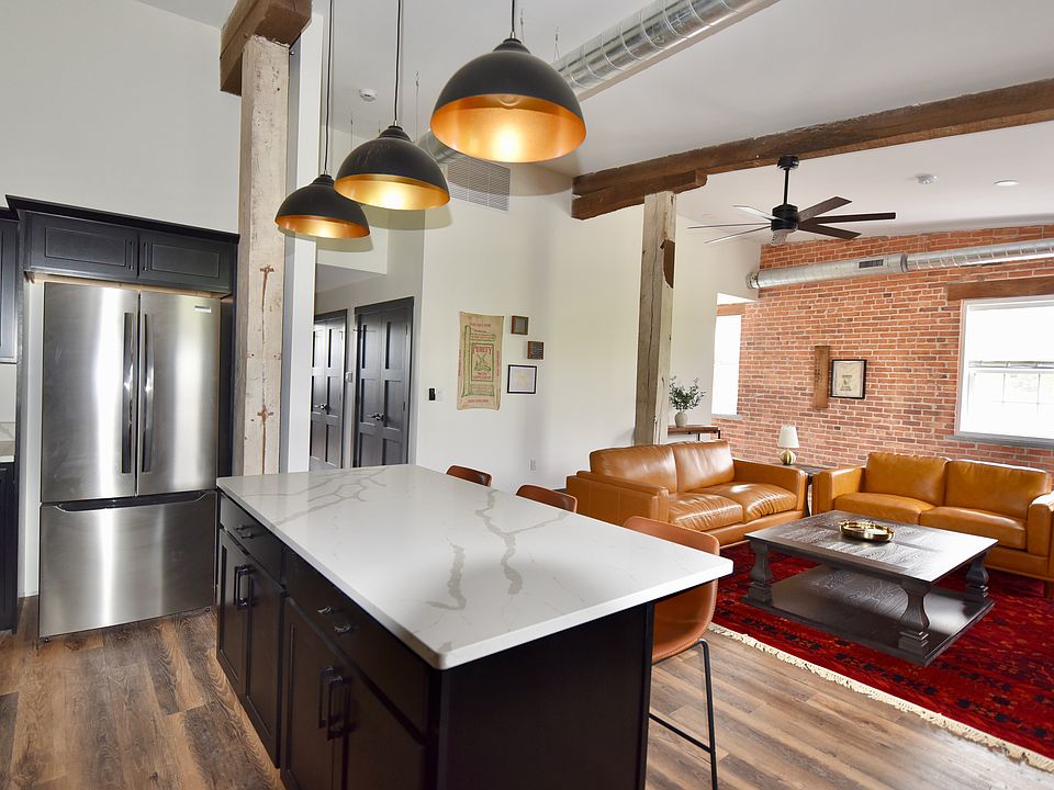 The living room features an open layout with optimal seating throughout, a desk/work space and a smart TV. The room features ceiling spotlights that are dimmable (its a whole mood) and a ceiling fan.