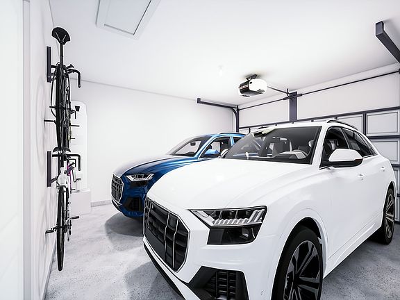 A white luxury SUV parked in a modern, well-lit garage with various tools and equipment visible in t