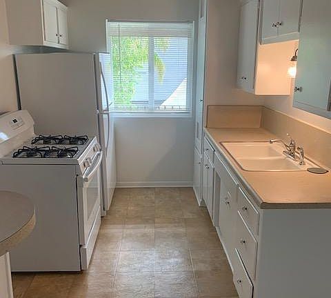Galley kitchen with stove, refrigerator and garbage disposal.