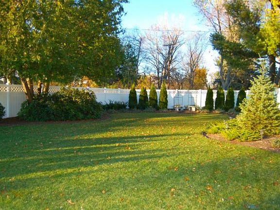 The new design includes white privacy fencing, full sprinkler system, shrubs, and new lawn.