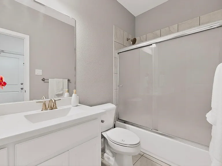 A clean bathroom featuring a shower, toilet, and vanity, with neutral-colored tiles and bright lighting.