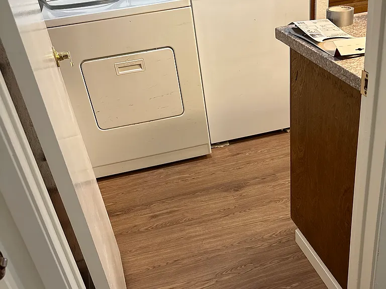 Full size washer and dryer, in enclosed laundry room, which includes amble shelving for additional storage.