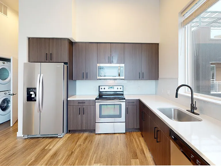 Apartment kitchen with stainless steel appliances, quartz countertops and wood-style flooring.