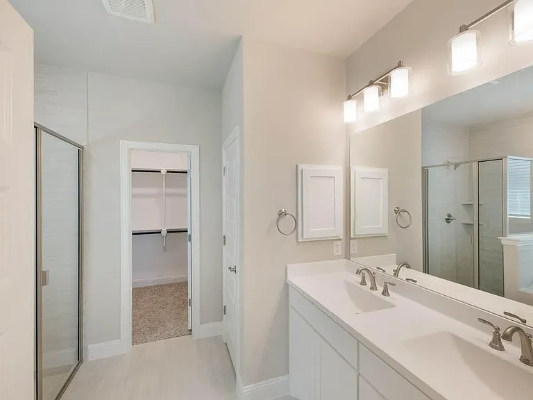 Bathroom featuring a dual vanity with a large mirror, shower enclosure with glass door, and a built-in linen cabinet