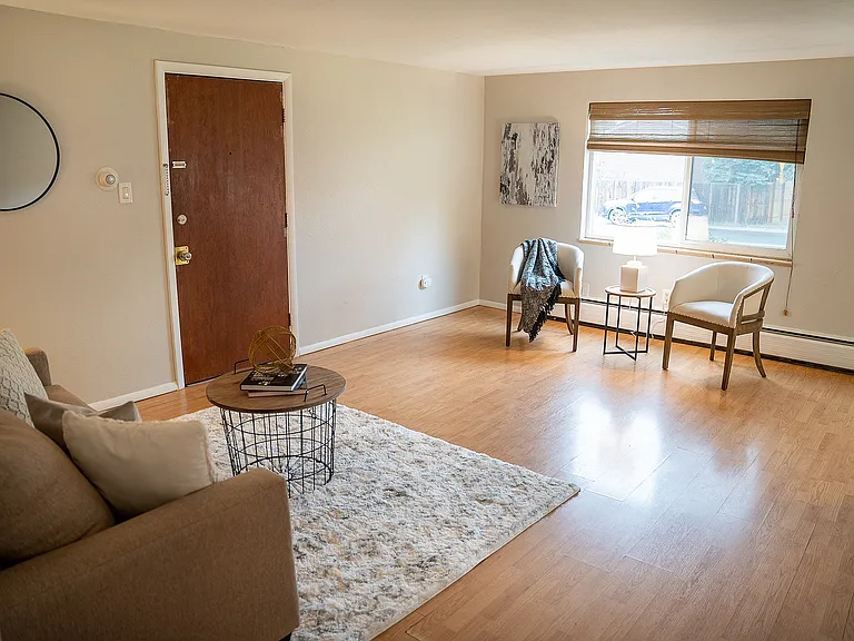 Inviting living room with warm wood flooring, modern furnishings, cozy seating area, and ample natural light through a large window.