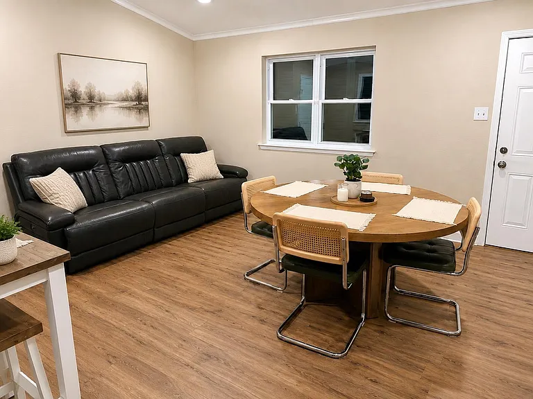 Open-concept common area with a dining table for four and a comfortable sofa, plus durable flooring and a large window.
