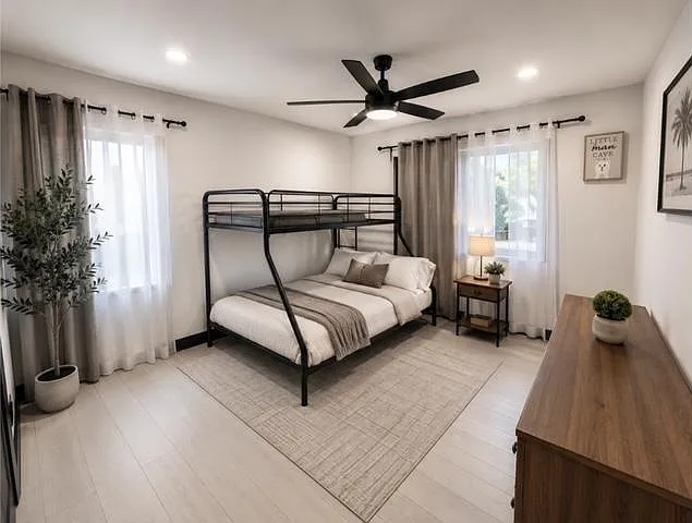 Spacious bedroom with a bunk bed, two windows with curtains, ceiling fan, and a dresser for convenient storage.