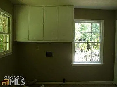 Laundry room with washer dryer hook-up, cabinet above and pantry to the right. The window on left looks out at backyard and the window on far wall looks out over driveway.