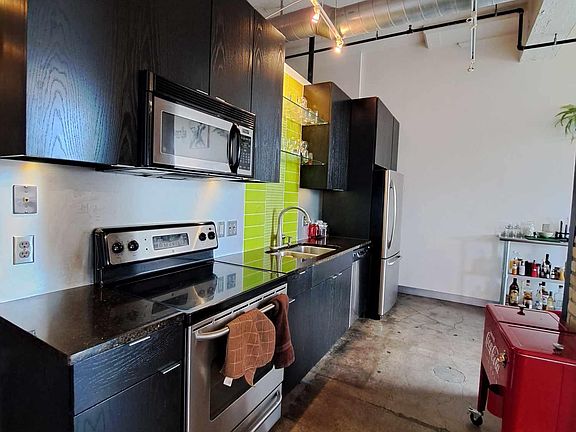 Gorgeous kitchen with bright green tiling, granite counters, stainless steel microwave, stove/oven, refrigerator, and dishwasher.