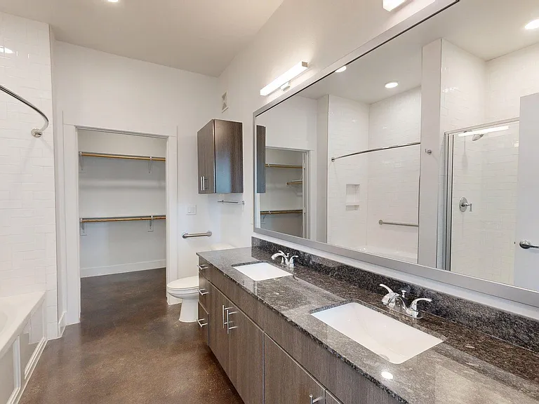 Apartment bathroom with large soaking tub, polished concrete flooring, and double sinks.