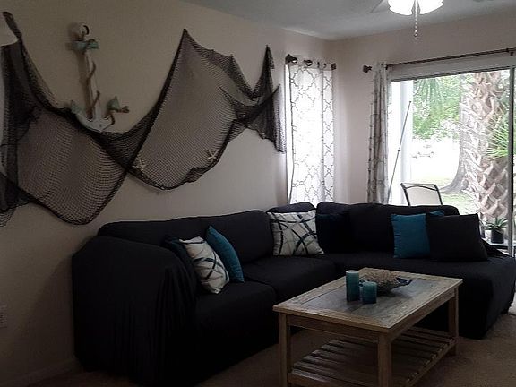 The Living Room with comfortable sofa-chase lounge, fishing net and anchor decor on wall and view out the sliding door and porch to the back yard.