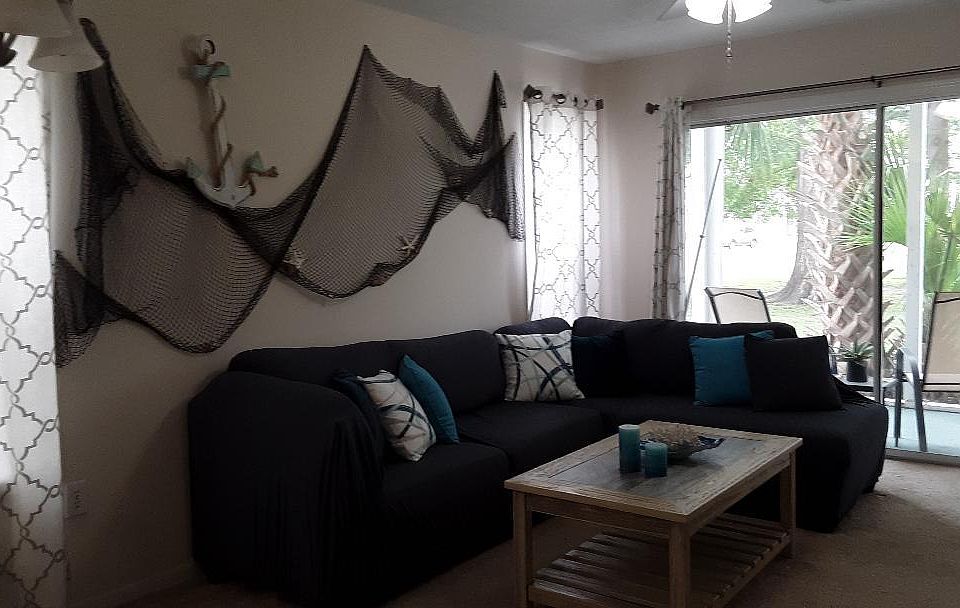 The Living Room with comfortable sofa-chase lounge, fishing net and anchor decor on wall and view out the sliding door and porch to the back yard.