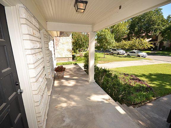 Covered front porch featuring a black paneled entry door, white brick facade, concrete flooring, and a beadboard ceiling.
