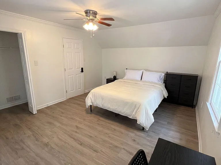 Spacious bedroom with wood-look flooring, ceiling fan, window light, and room for a bed plus a work desk.