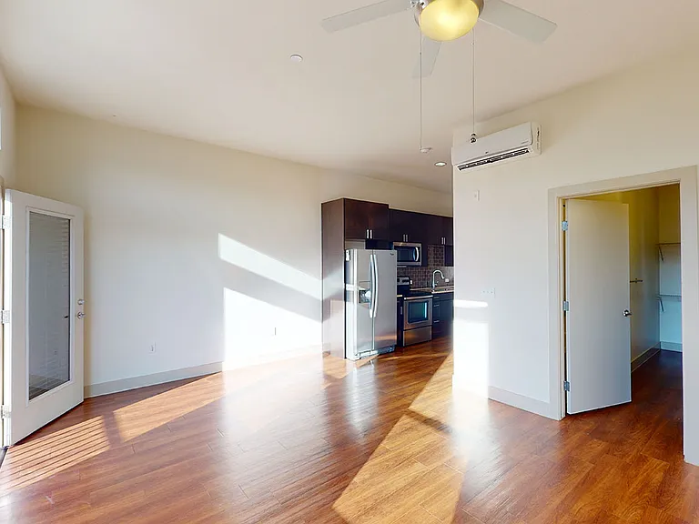 Apartment kitchen with stainless steel appliances and living room with wood-style flooring.