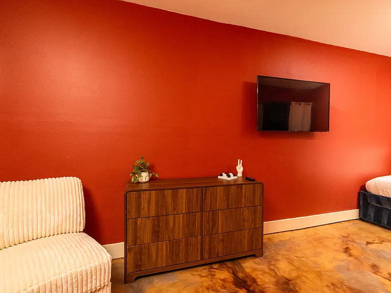 Warm and inviting bedroom featuring rich terracotta walls, a plush bed with colorful pillows, and a mounted TV_perfect for a cozy night in.