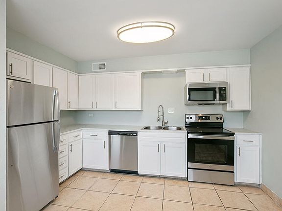 Modern kitchen with stainless steel appliances, white cabinetry, and sleek tile flooring.