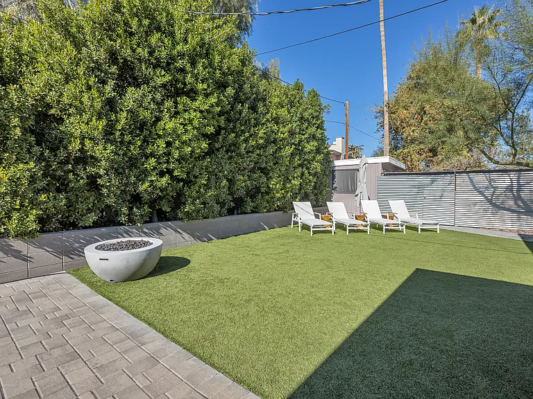 Expansive grassy backyard with mature ficus trees for privacy, gas fireplace, and sun loungers for outdoor relaxation