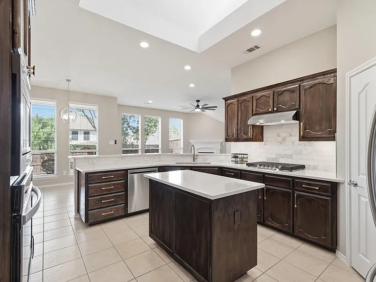 Expansive kitchen featuring dark wood cabinetry, white countertops, tile flooring, stainless steel appliances, and a central island