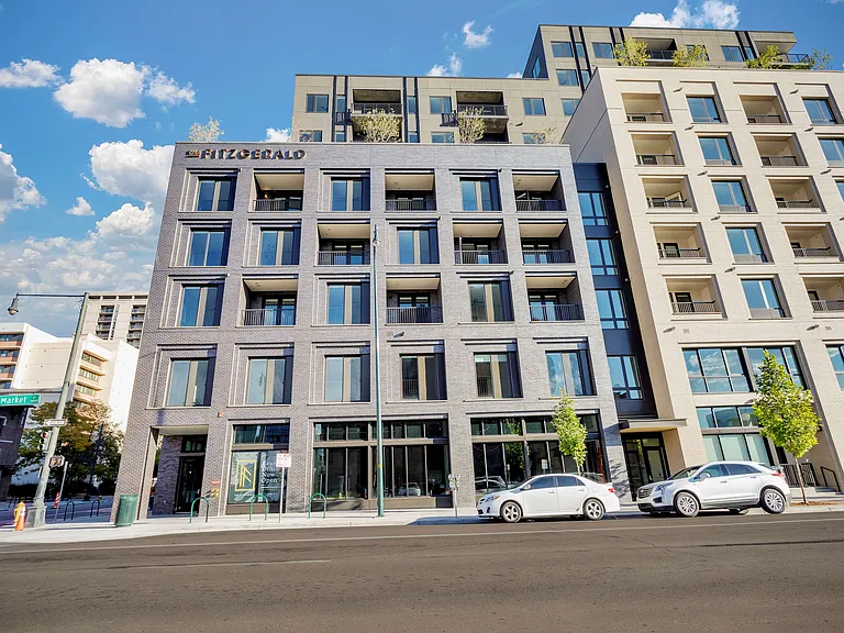 Modern urban apartment building featuring sleek architecture with large windows and balconies, set against a bright blue sky.
