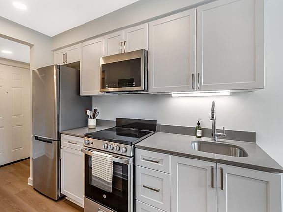 Renovated Package II kitchen with stainless steel appliances, light grey quartz countertops, white shaker cabinetry, and hard surface flooring