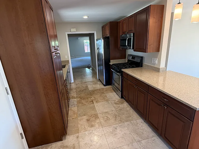 View of galley kitchen with excellent, and clean cabinetry, pantry, gas stove, pendants over clean granite countertop