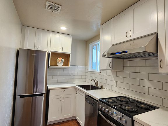 2-year-old remodeled kitchen with white cabinets, white tile backsplash, recessed lights, stainless steel refrigerator and stove.