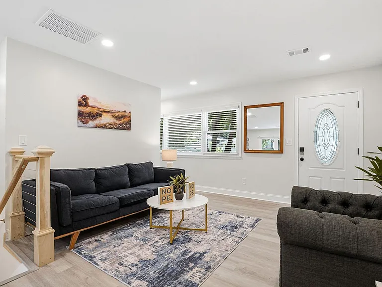Inviting living room with ample seating, recessed lighting, and large windows near the front entry and stairway.