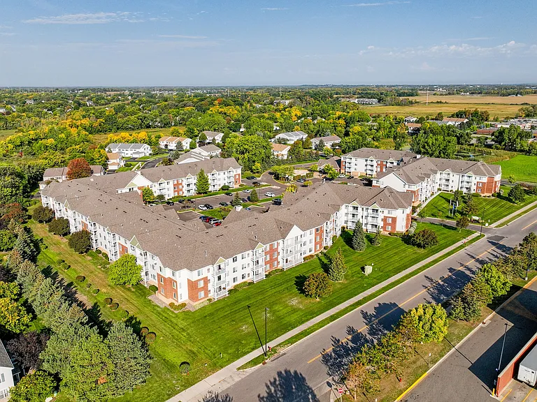 Aerial view of a modern apartment complex with spacious parking, lush greenery, and well-maintained surroundings.