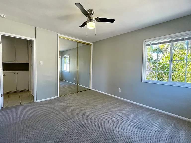 Bedroom with large closet, lots of natural light from west and north facing dual paned windows. View into the hallway with linen cabinet and utility cabinet.