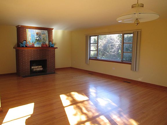 Oak floors & fireplace in living room overlooking yard.