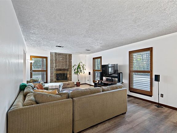 Large family room with several windows with shutters that bring a lot of light into the room. Wood burning fireplace.