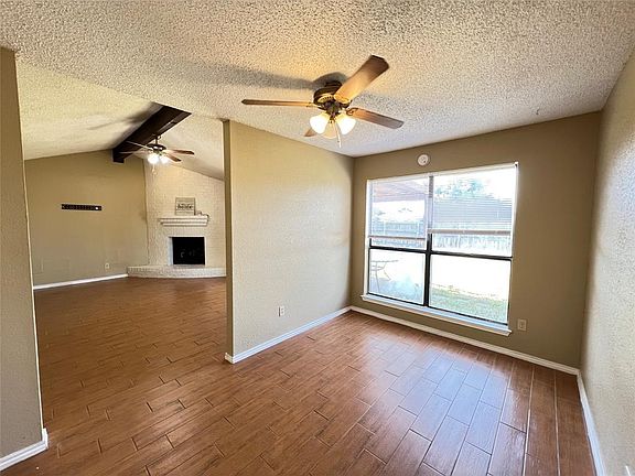 Unfurnished living room with brick wall, vaulted ceiling, a fireplace, dark hardwood / wood-style floors, and ceiling fan