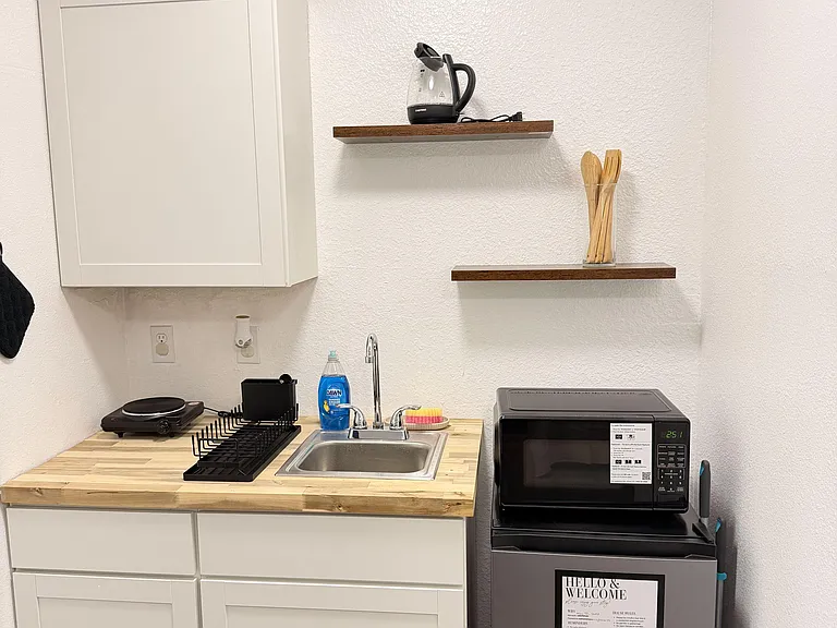 Compact kitchenette with butcher-block counters, sink, open shelving, and space for microwave and mini fridge.
