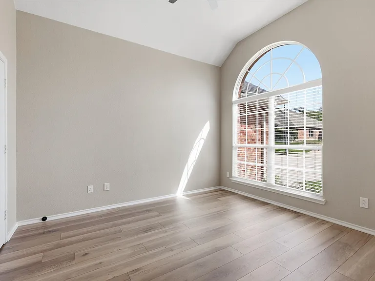 Vaulted ceiling with an arched window featuring blinds and light wood-finish flooring