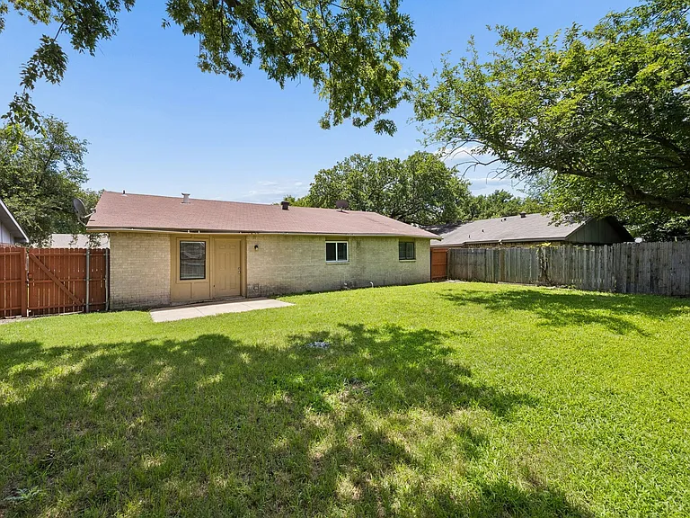 Spacious backyard with a large grass lawn, mature perimeter trees, and wood fencing