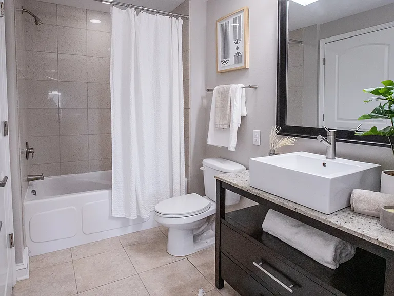 A stylish bathroom with elegant finishes from tile floor, square boutique sink above a granite countertop, and a chic tile tub surround, creating an elegant and functional space.