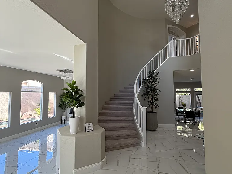 Elegant foyer highlighting the curved staircase, chandelier, and polished porcelain tile flooring.