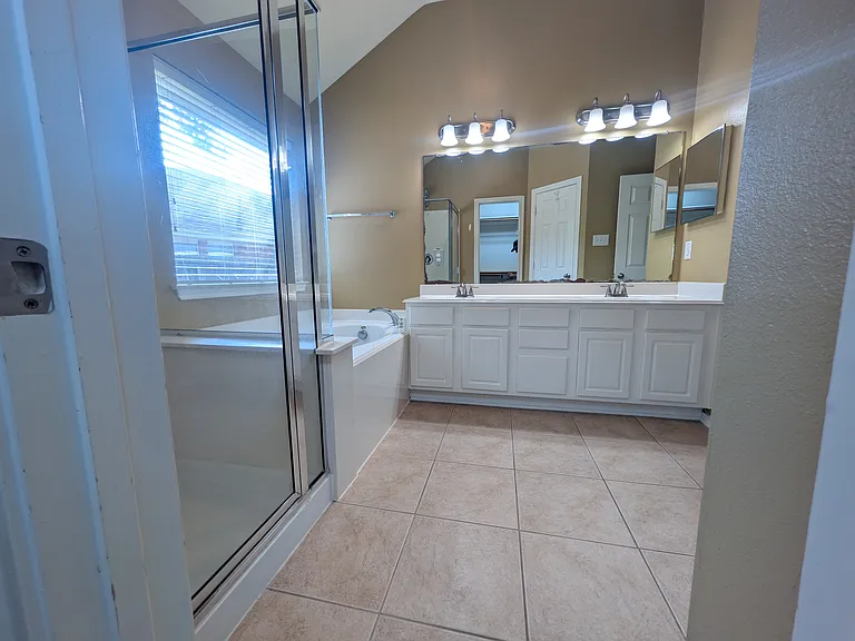 An inviting view showing the expansive double-sink vanity with abundant cabinet storage, dual vanity lighting, and clean tile flooring throughout.