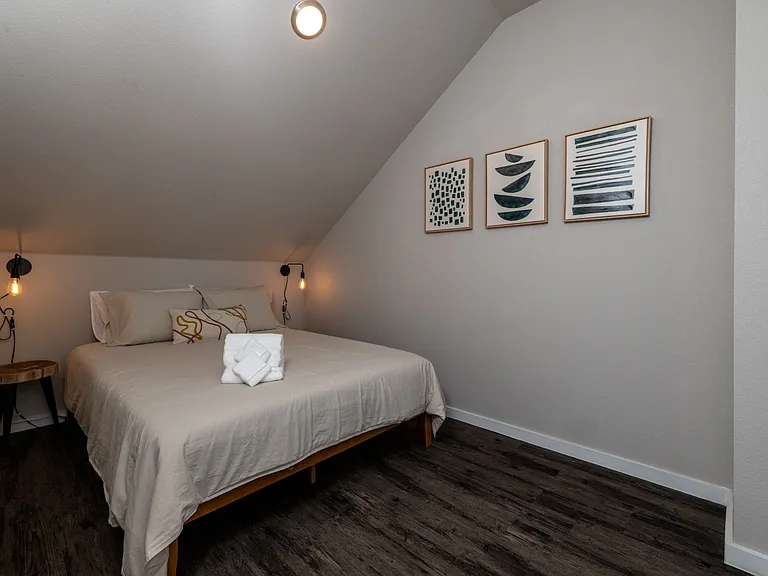 Charming fifth bedroom with a queen bed, cozy sloped ceiling, and warm hanging lights on each side_perfect for a restful, intimate vibe. This bedroom is located upstairs.