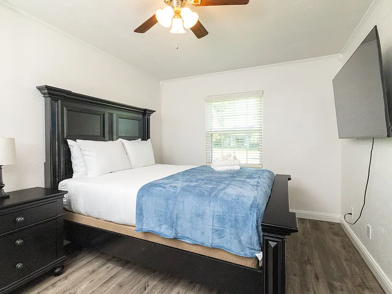 Bedroom 3 boasts a queen sized bed, cozy wood bed frame and headboard, a flat-screen Roku TV, and a comfy love seat_creating a peaceful and inviting space to relax and unwind. There is an attached closet with hangers and a luggage rack.