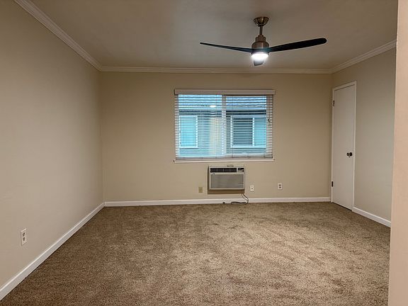 Studio living space: ceiling fan, AC unit under energy efficient living room window, closet on right.